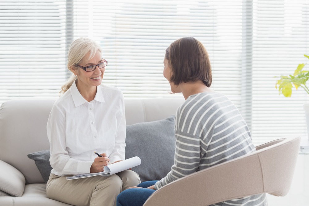 Smiling therapist with woman on sofa at home