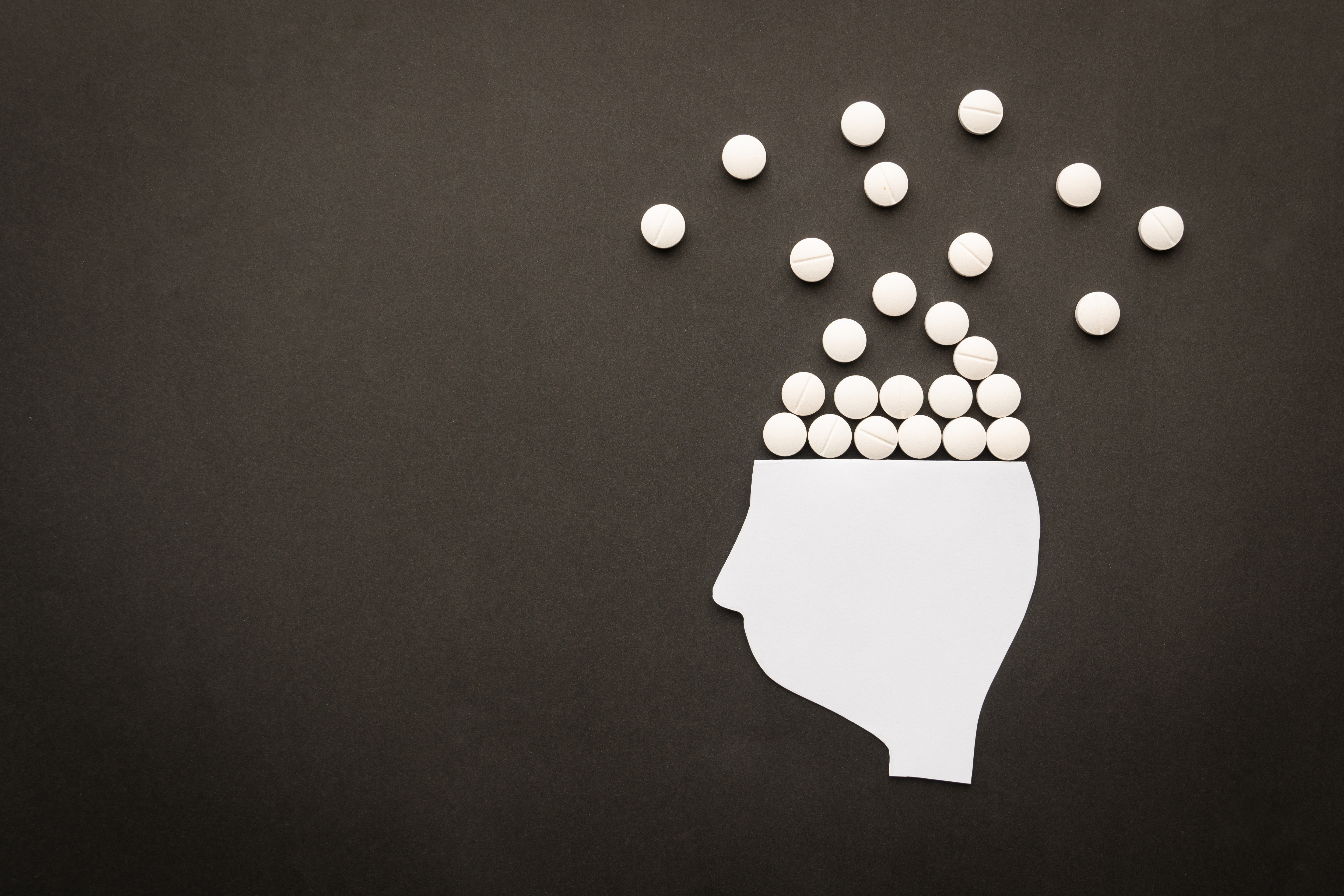 Drugs addiction and mental withdrawal symptoms concept. Human head with white pills on black background. International Day against Drug Abuse. Opioid use disorder concept