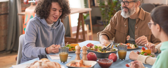 Happy family talking to each other while sitting at the table and having dinner at home
