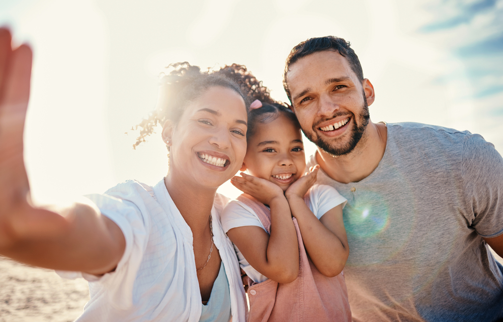 A joyful family captures a selfie together on the beach, smiling against a scenic ocean backdrop.