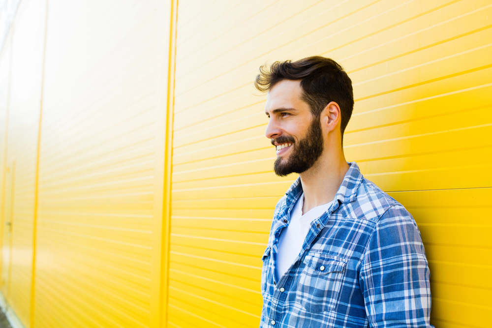 Happy man smiling, leaning against a bright yellow wall with horizontal lines. 